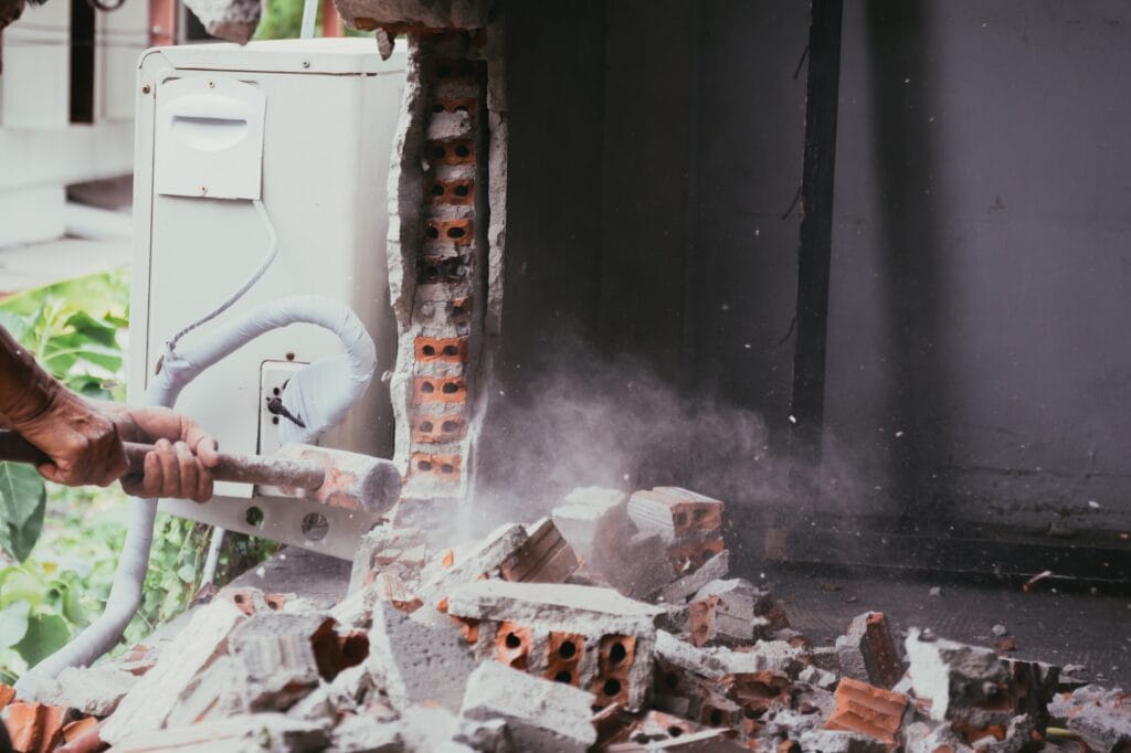 Unrecognizable builder using a sledgehammer breaking and smashing the wall fallen into debris